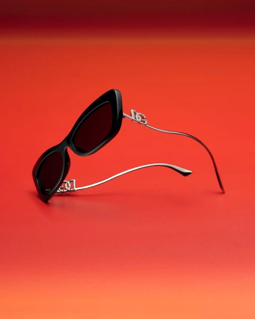 Angular black sunglasses with silver arms on a gradient red background. Close-up product shot for fashion accessories and eyewear.