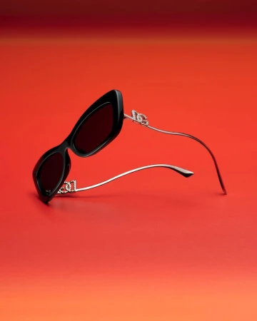 Angular black sunglasses with silver arms on a gradient red background. Close-up product shot for fashion accessories and eyewear.