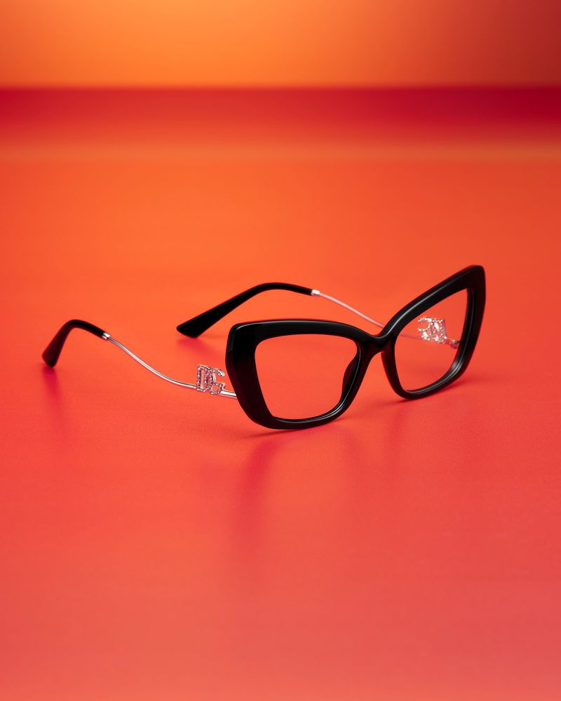 Black cat-eye glasses with silver accents on a vivid gradient orange surface. A fashionable eyewear product shot with studio lighting.