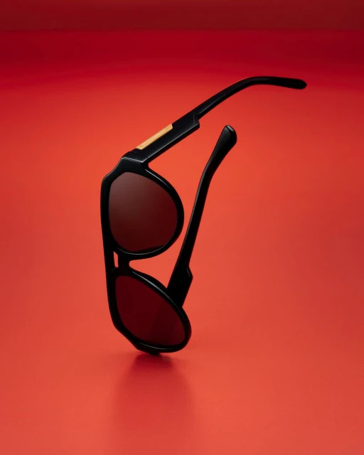 Black sunglasses with red lenses on red background. Product still life. Minimalist aesthetic. Eye protection and fashion accessory.