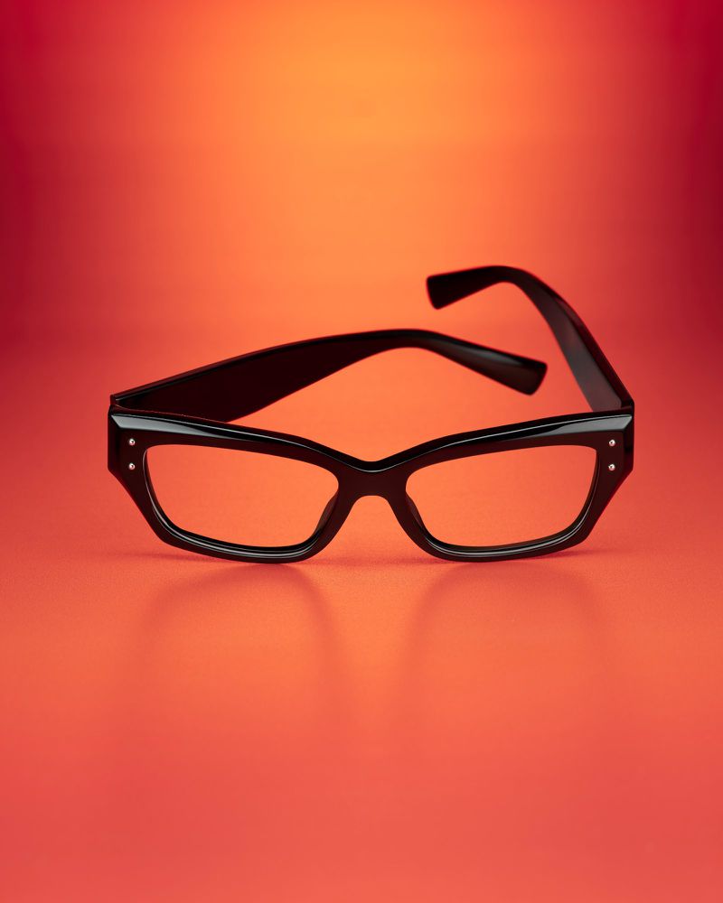 Eye-level studio shot of black-rimmed eyeglasses on a red and orange gradient background with subtle shadows. Product photography.