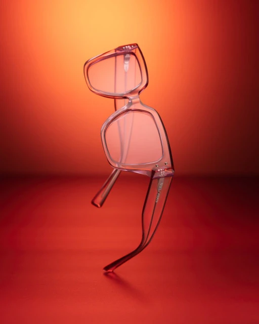 Close-up studio shot of transparent-frame eyeglasses with orange gradient background, showcasing eyewear design and product photography.