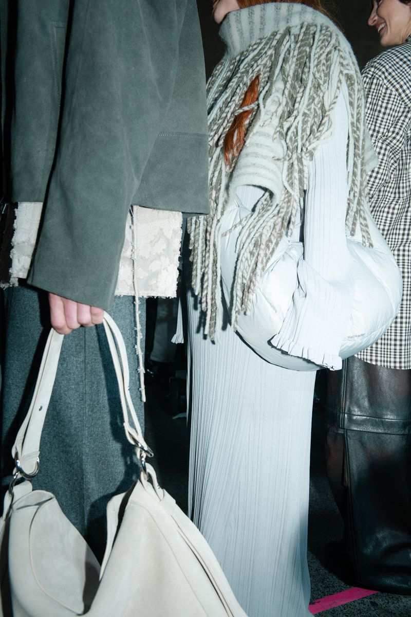 Three fashionably dressed adults with unique sweater textures and light-colored bags stand in an indoor setting with soft, diffused lighting.