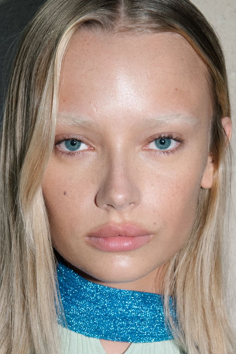 Close-up portrait of a fair-skinned adult woman with light blonde hair and striking blue eyes, wearing a turquoise choker necklace.