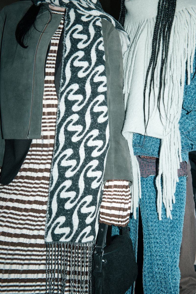 Fashionable women's clothing including scarves, jackets, and dresses featuring patterns and textures in an indoor setting. 