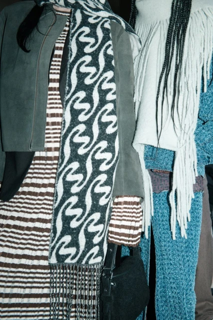 Fashionable women's clothing including scarves, jackets, and dresses featuring patterns and textures in an indoor setting. 
