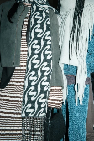 Fashionable women's clothing including scarves, jackets, and dresses featuring patterns and textures in an indoor setting. 