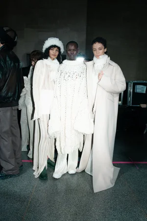 Three models wearing cream and white winter knitwear and outerwear backstage at Holzweiler AW24