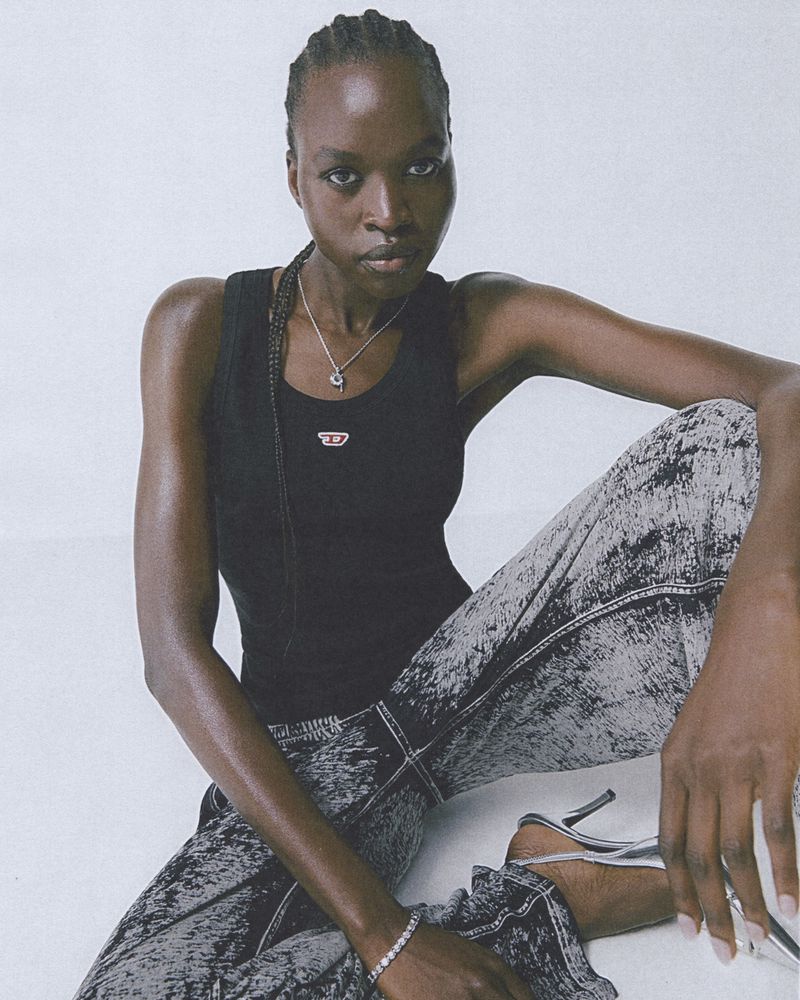 Fashion portrait of a Black female model in a black tank top and acid wash jeans, posing in a studio with silver heels.