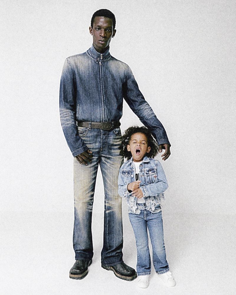 Adult male and child posing together, both wearing denim outfits in a studio setting. The child is yawning with their hand to their chest.