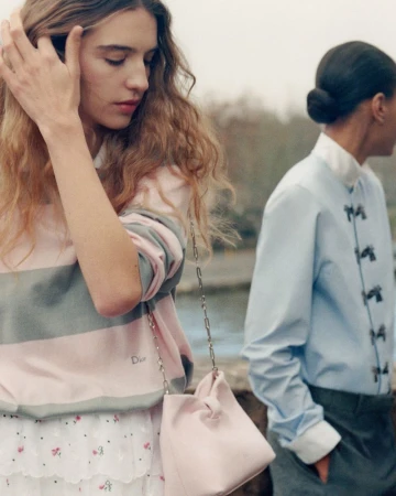 Two female models posing outdoors, one wearing a striped pink sweater and carrying a pink handbag, another in a light blue shirt.