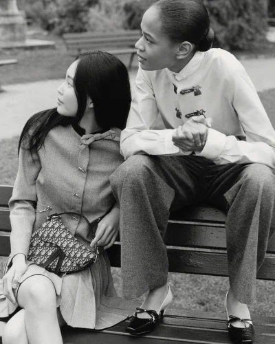 Two female models seated on a park bench wearing Dior collection attire in a black and white photograph