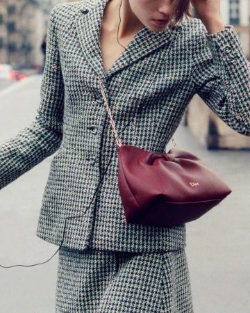 Model wearing houndstooth blazer and matching skirt with a burgundy handbag outdoors on a street