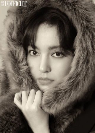 Close-up portrait of an East Asian woman wearing a plush fur hood holding the collar against a neutral background.