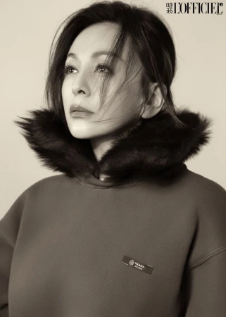 Monochrome portrait of an East Asian woman wearing a dark hoodie with a black fur collar against a studio background.