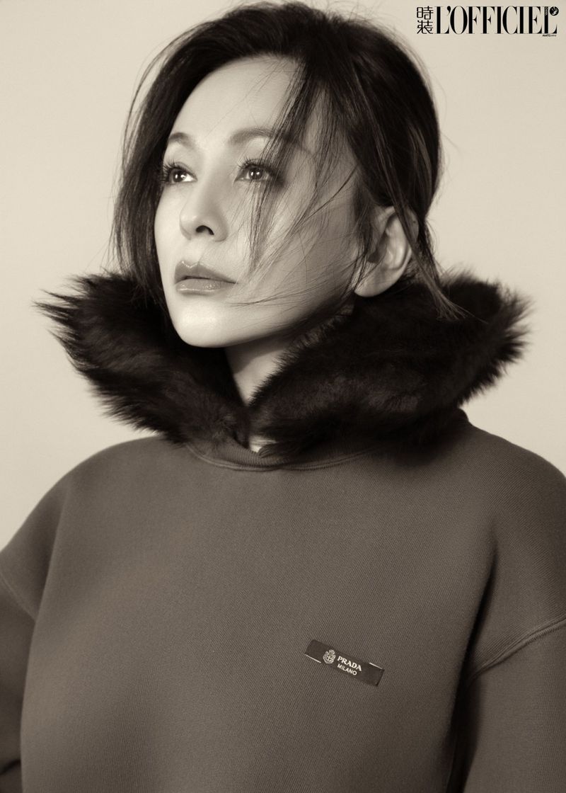 Monochrome portrait of an East Asian woman wearing a dark hoodie with a black fur collar against a studio background.