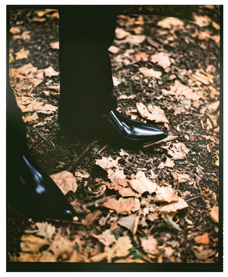 Fashionable black patent leather heeled shoes on autumn leaves in a woodland setting, creating a stylish and seasonal image.