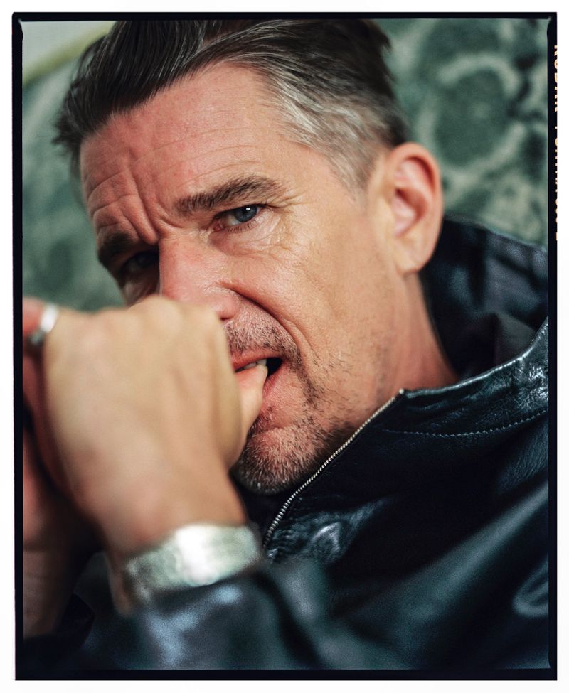 Portrait of a mature man with gray hair wearing a black leather jacket, biting his fingers and looking intensely at the camera.