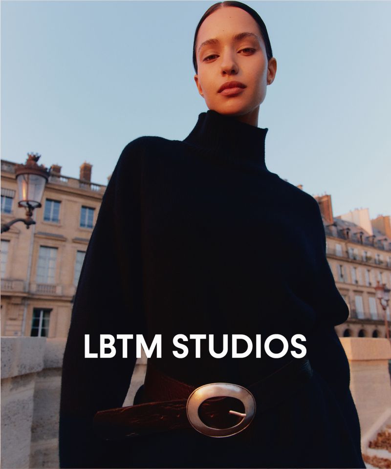 Fashion portrait of woman in black turtleneck sweater with Paris buildings in the background taken at eye-level under blue sky.
