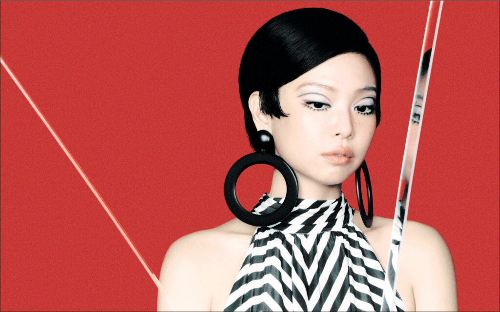 Woman with mod hairstyle and zebra-print top poses against a red background with large hoop earrings in a fashion-forward image.
