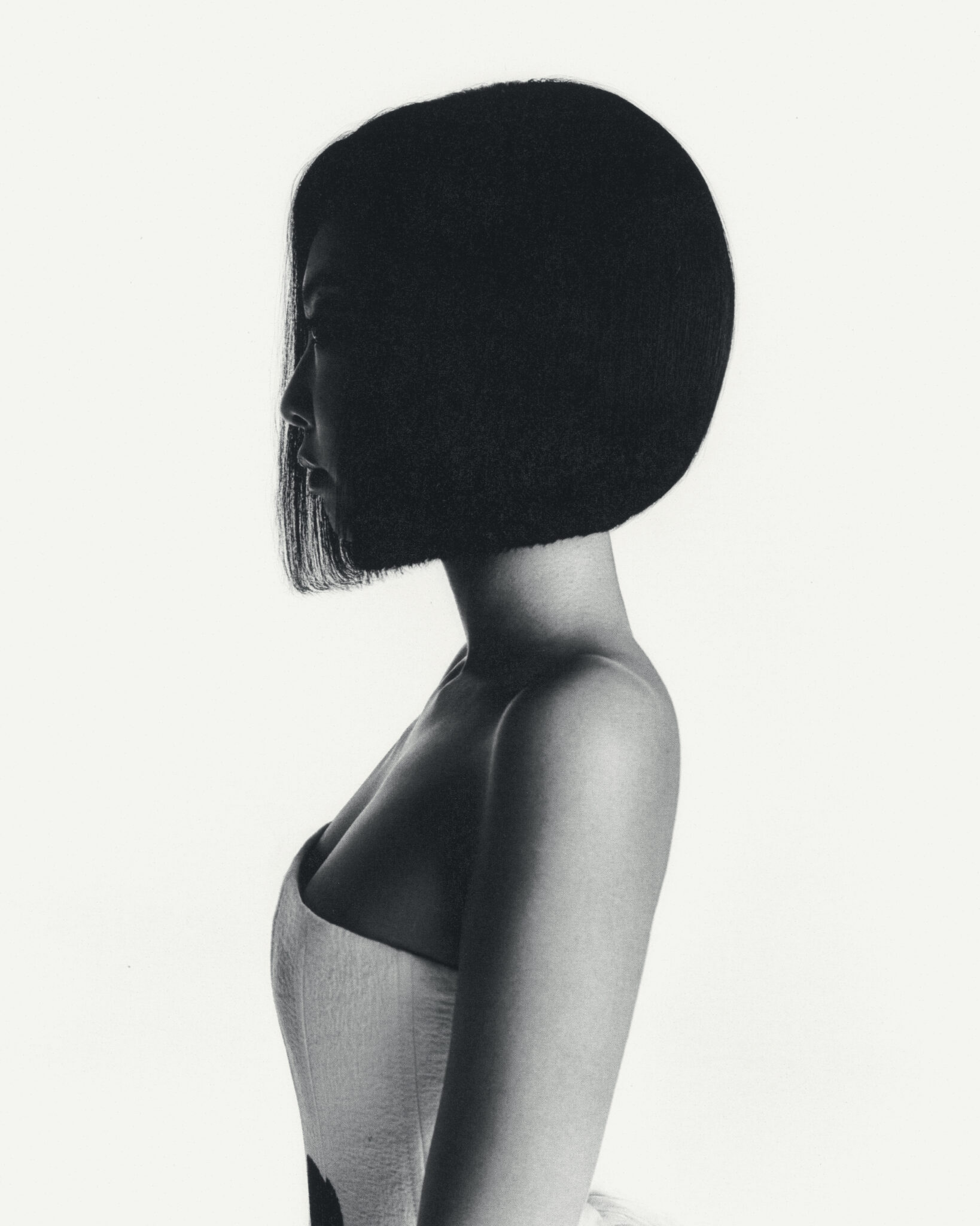 Striking black and white portrait of a woman with a sleek bob hairstyle, wearing a strapless top against a clean, bright backdrop.