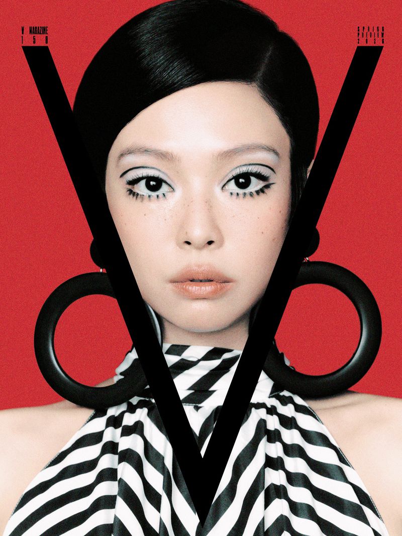 Close-up portrait of Jennie in a black and white striped halter top against a solid red background with large sculptural black earrings