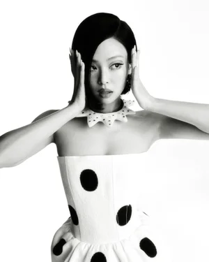 Jennie wearing a white polka dot strapless dress and spiked collar with hands framing her face in a high-contrast portrait for V Magazine