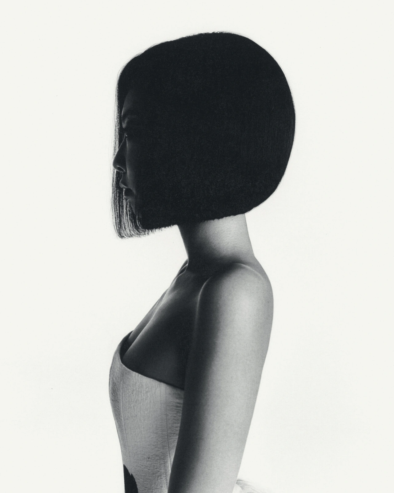 Profile portrait of a woman with a dark bob haircut wearing a strapless top against a white background
