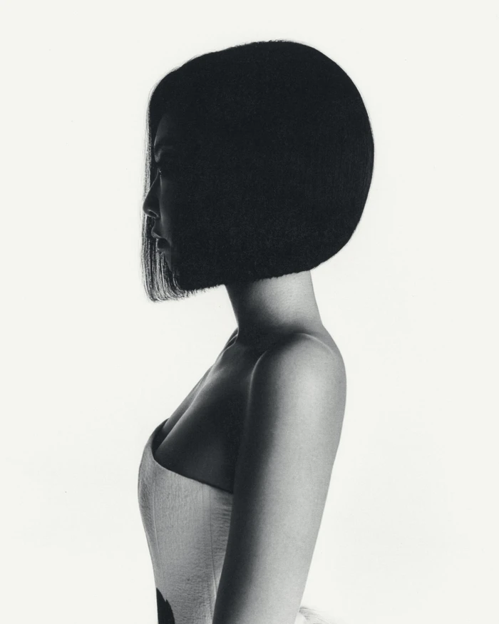 Profile portrait of a woman with a dark bob haircut wearing a strapless top against a white background
