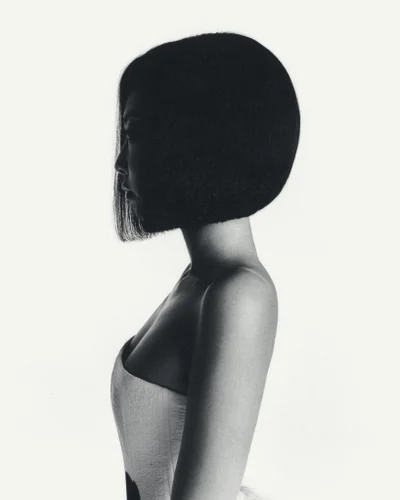 Profile portrait of a woman with a dark bob haircut wearing a strapless top against a white background