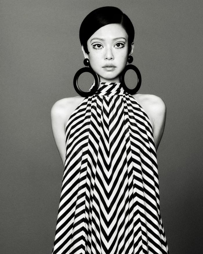 Black and white portrait of Jennie wearing a chevron halter dress and oversized circular earrings against a plain grey backdrop.
