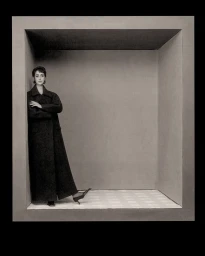 Model standing inside a large grey architectural frame wearing a dark coat and heels for The Cut December 2025 Special Issue