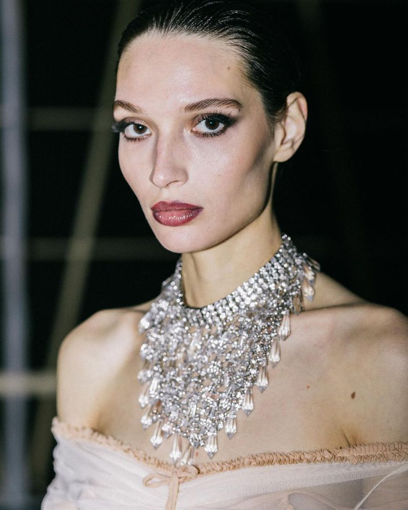 Elegant adult woman with slicked-back hair and a large crystal necklace in a studio setting. Fashion and beauty shot.