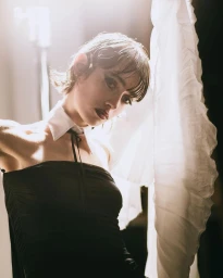 Model in a black strapless top with a white collar and tie against a bright studio background