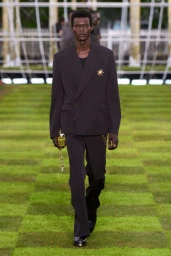Model in a dark suit walking on a checkered lawn during the Louis Vuitton runway presentation