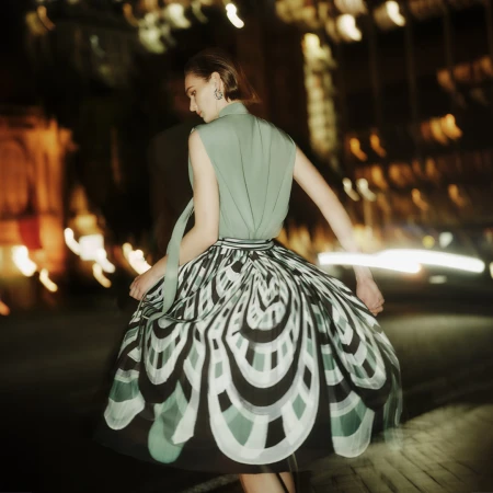 Model in green sleeveless top and patterned flared skirt on a blurred nighttime street for Perri Cutten