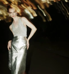 Model wearing a silver metallic top and skirt against a dark background with blurred light streaks.