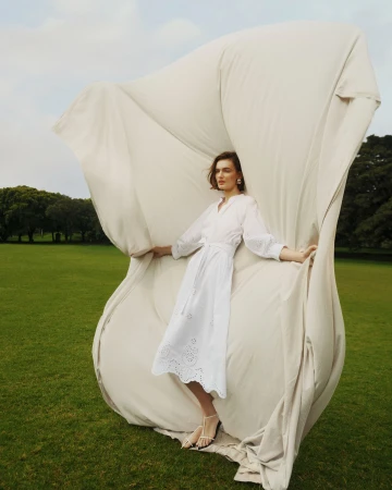 Model in white dress holding up a large billowing cream fabric sheet in an outdoor park setting