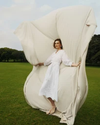Model in white dress holding up a large billowing cream fabric sheet in an outdoor park setting