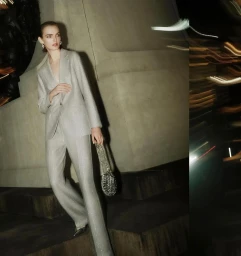Model in a silver pantsuit holding a metallic handbag against an architectural stone background at night.