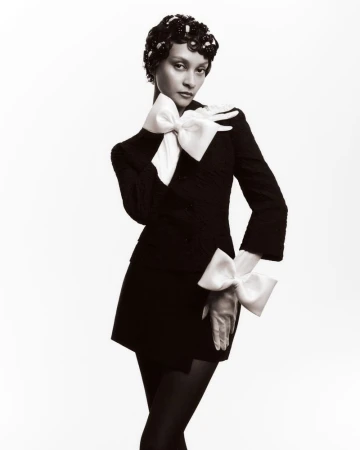 Portrait of an adult woman wearing a black dress with oversized white bows on the sleeves, posing against a white backdrop in a studio.