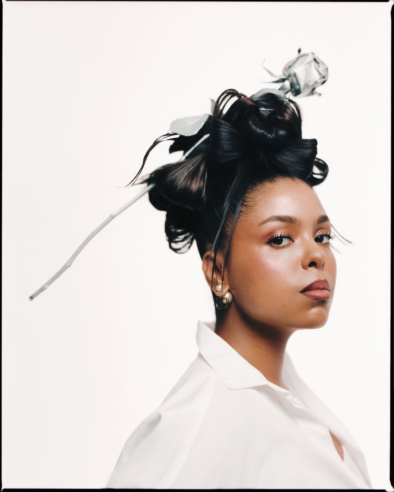 Headshot of a woman with an elegant updo hairstyle adorned with a silver flower, wearing a white button-down shirt against a white backdrop.