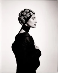 Profile portrait of a woman wearing a heavily embellished beaded cap with CD logo and a black coat against a plain background