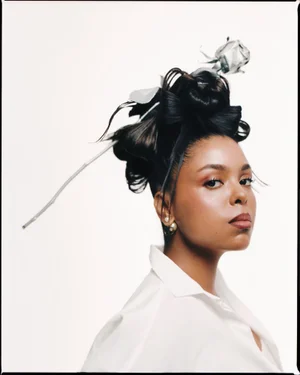 Woman in white shirt with elaborate dark hair styled with a silver rose accessory against a plain white background
