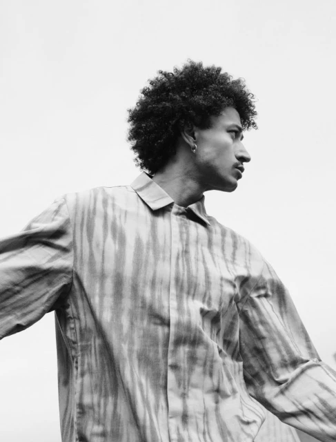 Portrait of an adult male with an afro hairstyle wearing an open striped shirt looking sideways against a white sky background.