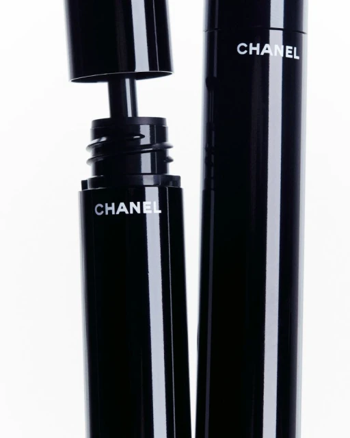 Black Chanel mascara tubes with white branding on a clean white background. One tube open with applicator visible. Beauty, makeup, product shot.