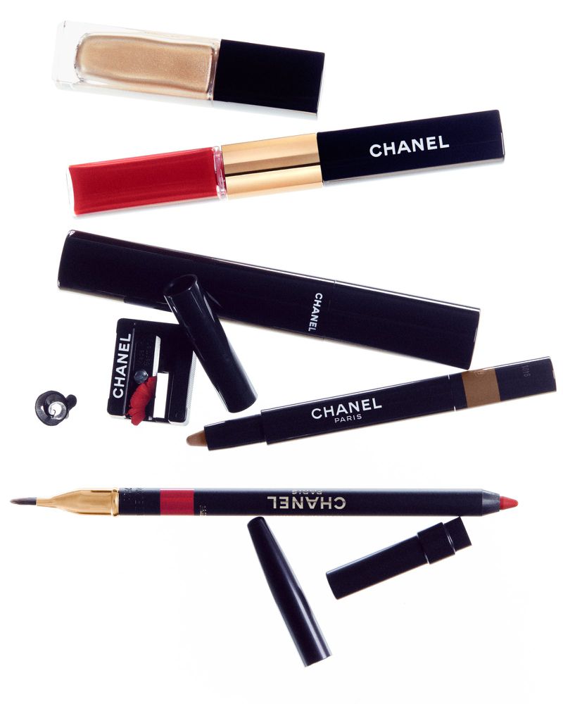 Assortment of Chanel lipsticks, eyeliners, and beauty products arranged on a white background in a visually appealing composition.