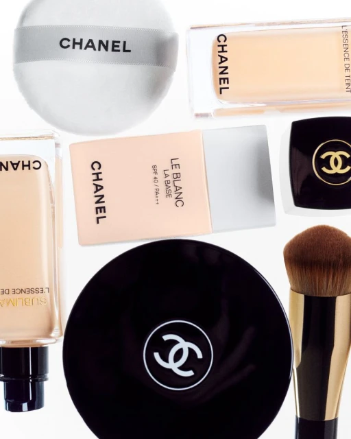 A collection of Chanel brand makeup products are displayed on a white background, showcasing foundation and powder compacts with logo.