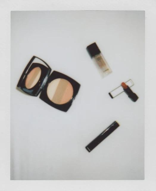 Overhead shot of face makeup, including powder compact, lipstick and foundation, on a white surface, simple product photography.