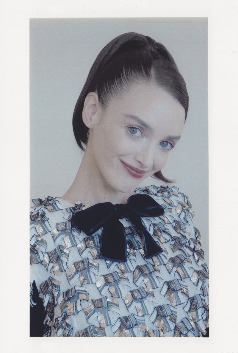 Portrait of an adult woman with dark hair pulled back, wearing a light patterned blouse with a large black velvet bow, smiling.